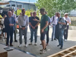 Eine Delegation mit 13 Männern steht vor einer Halle der Schreinerei Huber. Firmenchef Huber spricht zu Staatssekretär Dörflinger.
