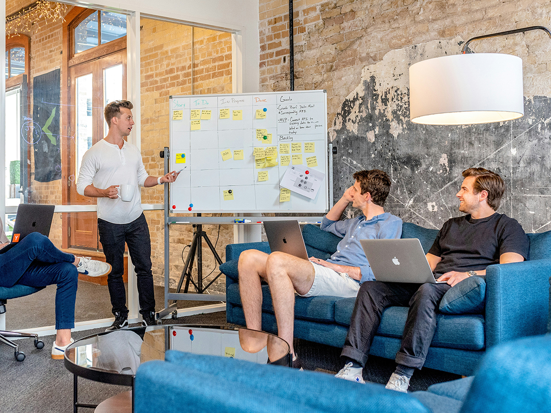 Junger Mann an Flipchart spricht zu drei anderen jungen Männern.