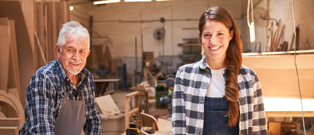 Älterer Schreiner und junge Schreinerin in einer Werkstatt.