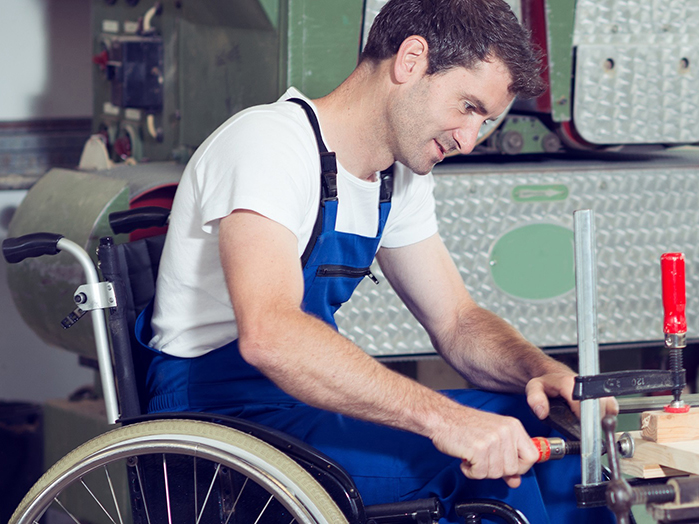 Rollstuhlfahrer arbeitet an Werkbank in Schreinerwerkstatt.